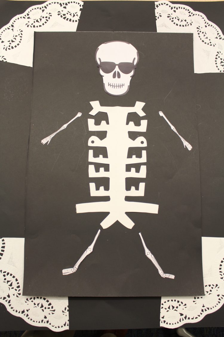 Skeleton made out of white construction paper against a black canvas