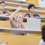 students hand raised in college lecture hall