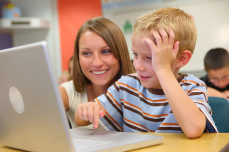 Elementary school student and teacher look at computer