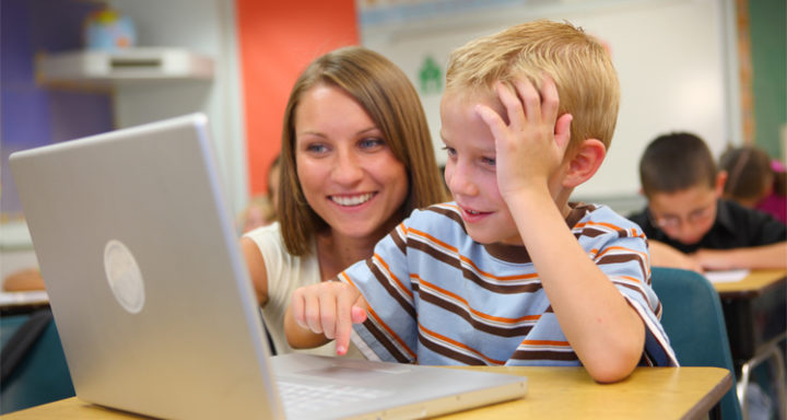 Elementary school student and teacher look at computer