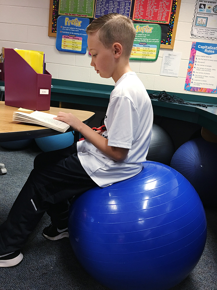 student using yoga ball as a chair in class
