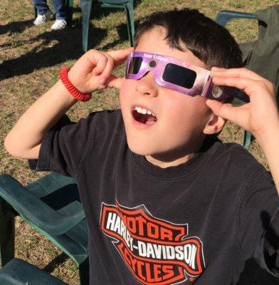 child wearing eclipse glasses looking surprised