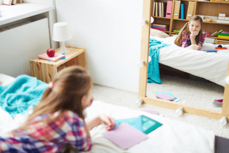 little girl laying on bed looking in mirror