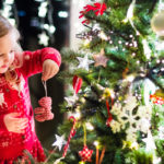 little girl hanging an ornament on Christmas tree