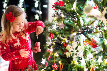 little girl hanging an ornament on Christmas tree