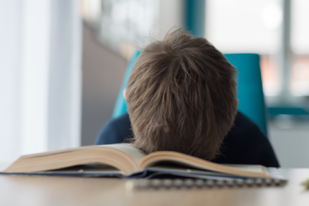 tired kid. resting head in open book on table