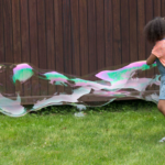 girl making a giant bubble in backyard