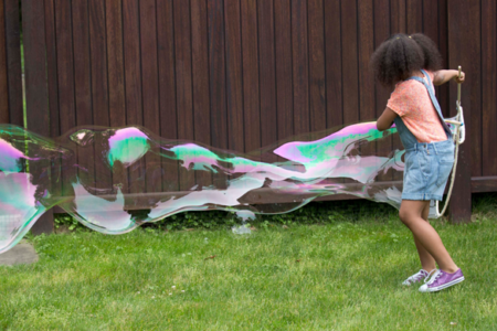 girl making a giant bubble in backyard