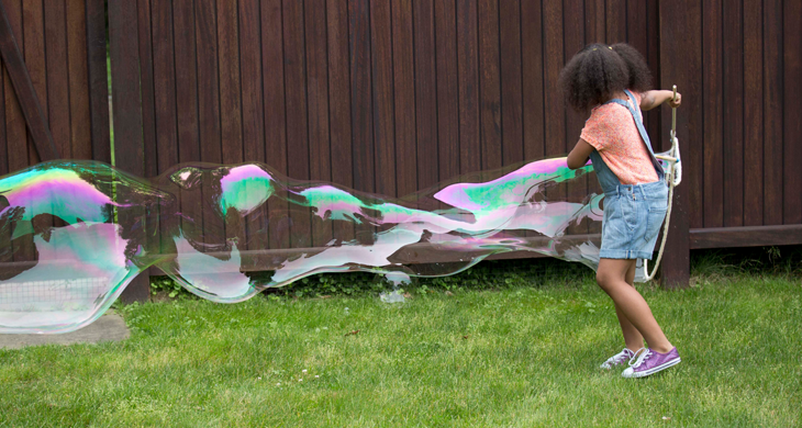 girl making a giant bubble in backyard