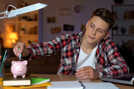 teen boy putting money in piggy bank