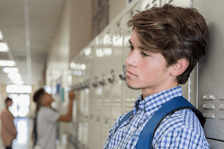 high school student leaning against locker with sad expression