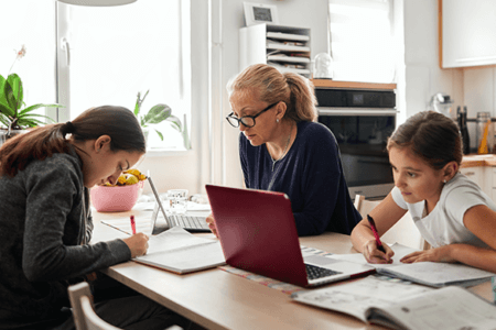 mother and her two daughters doing work and school work at a table together at home